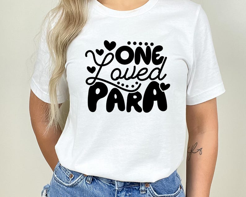 May include: White t-shirt with black text that reads "One Loved Para" with hearts around the text.