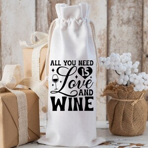 May include: White fabric wine bottle bag with black text that reads "All you need is love and wine" with a heart and wine glass graphic.