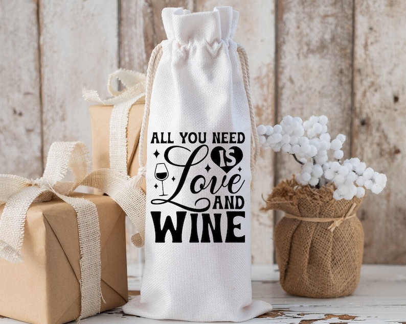 May include: White fabric wine bottle bag with black text that reads "All you need is love and wine" with a heart and wine glass graphic.