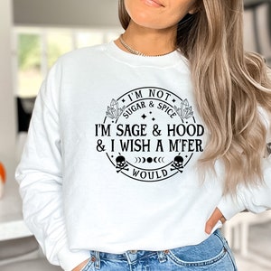 May include: White sweatshirt with a black graphic print that reads "I'm not sugar & spice I'm sage & hood & I wish a m'fer would". The graphic is a circle with a skull and crossbones, crystals, and stars.