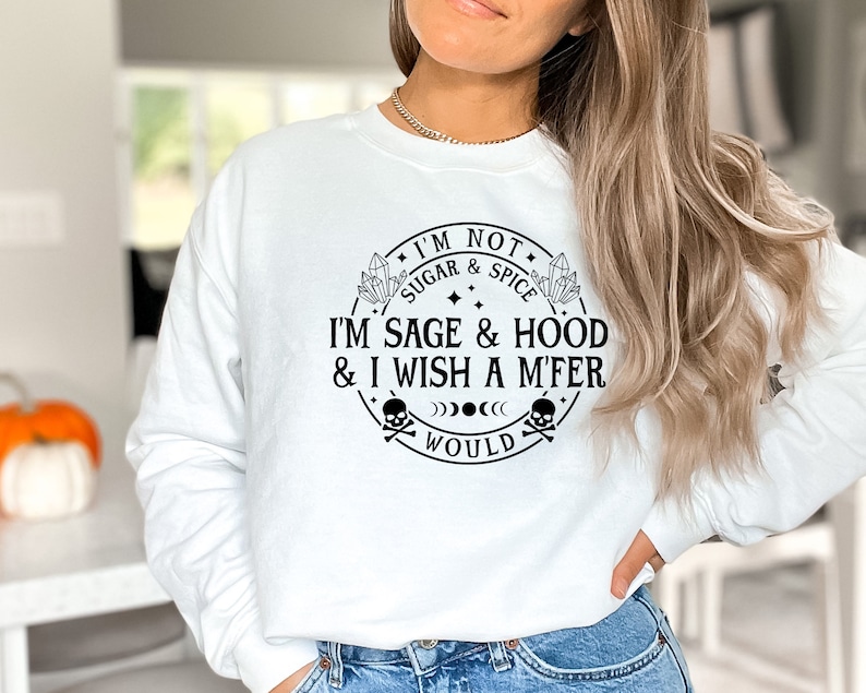 May include: White sweatshirt with a black graphic print that reads "I'm not sugar & spice I'm sage & hood & I wish a m'fer would". The graphic is a circle with a skull and crossbones, crystals, and stars.