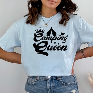 May include: A light blue t-shirt with a black graphic design that says "Camping Queen" with a crown, tent, and heart.