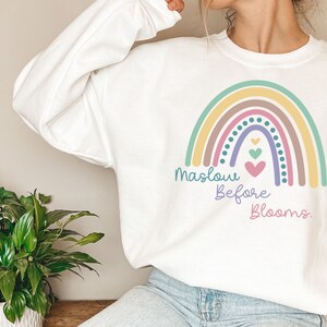 May include: White sweatshirt with a rainbow graphic and the text "Maslow Before Blooms."