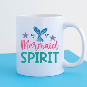 May include: White ceramic mug with a teal, pink and purple mermaid tail design and the text "Mermaid Spirit".