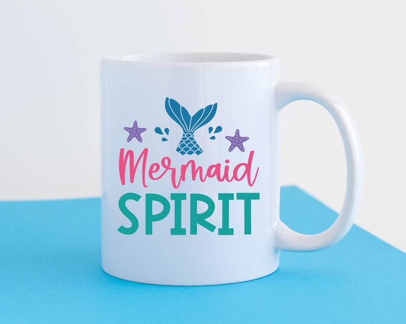 May include: White ceramic mug with a teal, pink and purple mermaid tail design and the text "Mermaid Spirit".