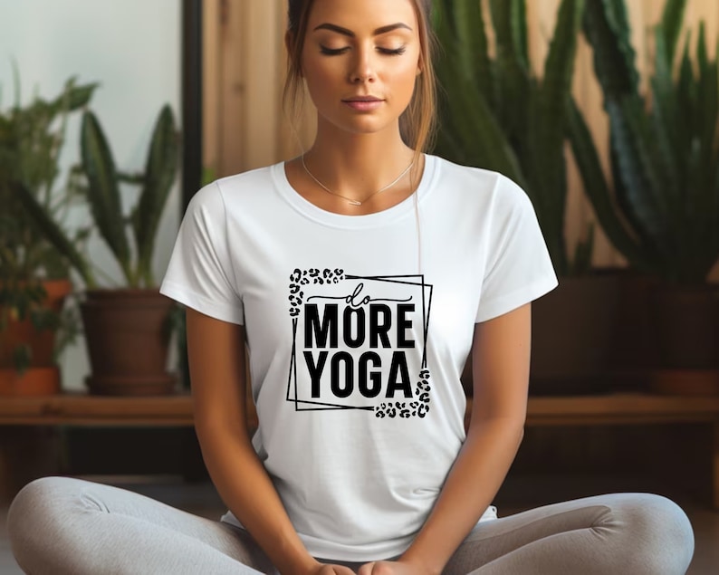 May include: A white t-shirt with a black graphic that says "do more yoga" inside a black frame with leopard print accents.