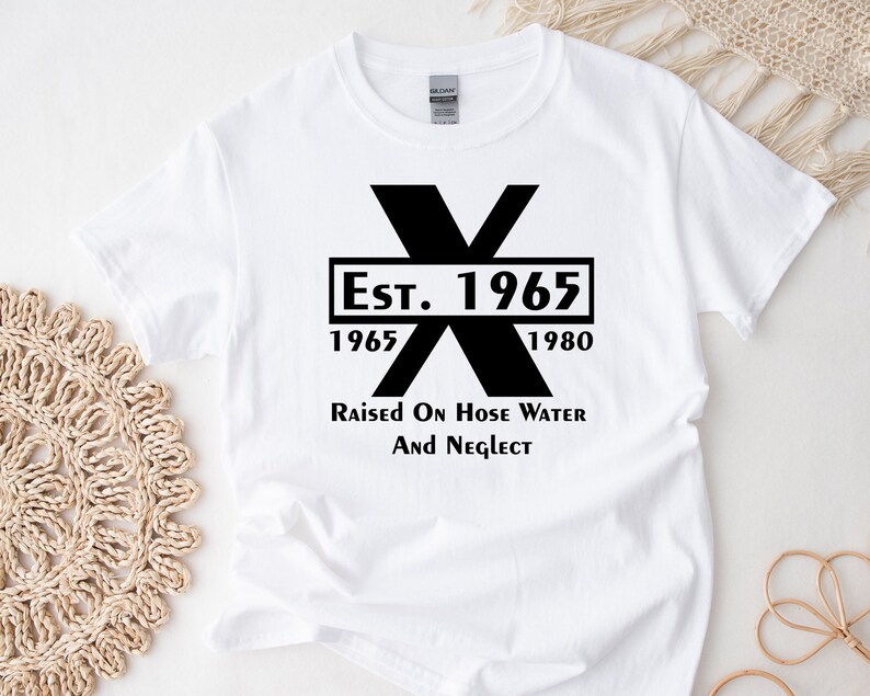 May include: White t-shirt with a black graphic design. The graphic features a large black X with the text "Est. 1965" and "1965" and "1980" below the X. The text "Raised on Hose Water and Neglect" is below the graphic.