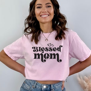May include: A pink t-shirt with the text "Blessed Mom" in black retro-style lettering and small hearts above the text.
