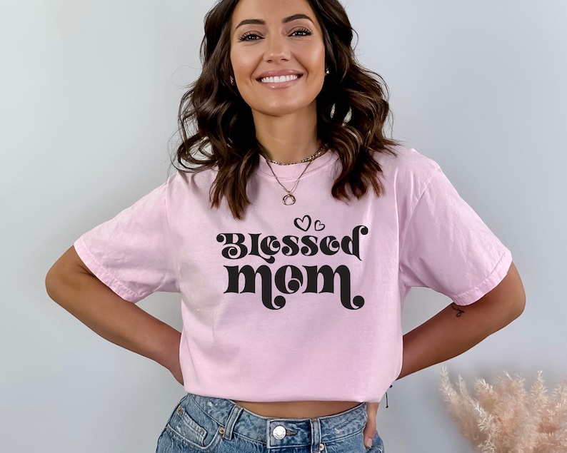 May include: A pink t-shirt with the text "Blessed Mom" in black retro-style lettering and small hearts above the text.