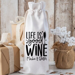 May include: White fabric wine bottle bag with black text that reads "Life is good wine. Make it better."