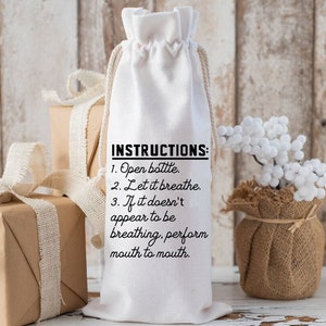 May include: White fabric wine bottle bag with black text that reads "INSTRUCTIONS: 1. Open bottle. 2. Let it breathe. 3. If it doesn't appear to be breathing, perform mouth to mouth."