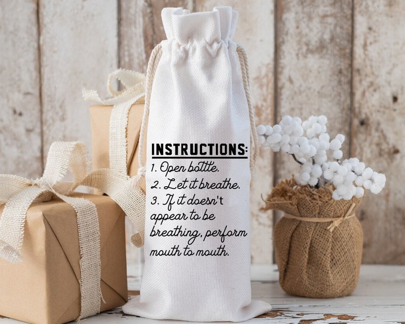 May include: White fabric wine bottle bag with black text that reads "INSTRUCTIONS: 1. Open bottle. 2. Let it breathe. 3. If it doesn't appear to be breathing, perform mouth to mouth."
