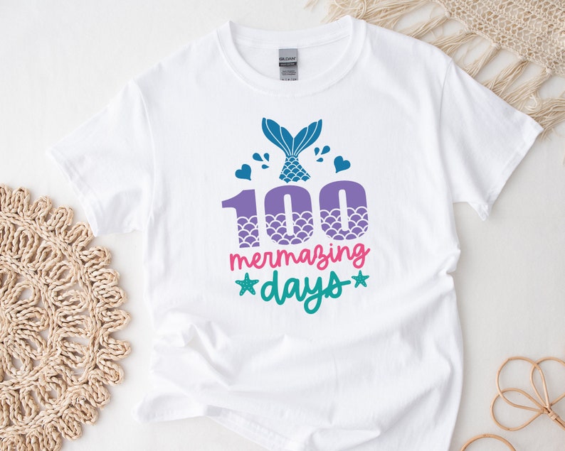 May include: White t-shirt featuring a mermaid tail graphic and the text "100 mermazing days" in pink, green, and purple.