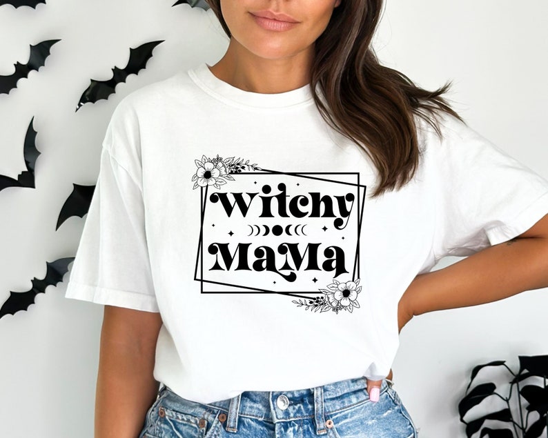 May include: White t-shirt with black text that reads "Witchy Mama" in a retro font. The text is framed by a black square with floral accents.