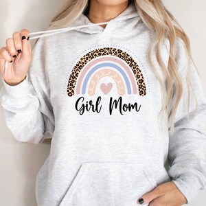 May include: A gray hoodie with a rainbow design featuring a pink, blue, and white rainbow with a leopard print border. The rainbow has a pink heart in the center and the text "Girl Mom" below it.
