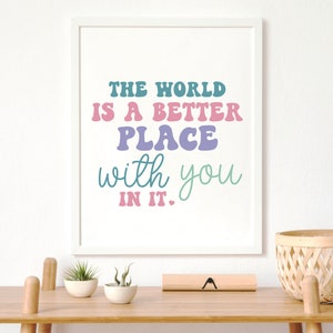May include: A white framed print with the text "The world is a better place with you in it." The text is in a colorful, retro font.