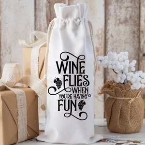 May include: White fabric wine bottle bag with black text that reads "Wine Flies When You're Having Fun" with a grape design.