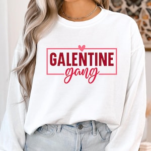 Op de afbeelding: Witte longsleeve trui met een rode doos en een roze hartgrafiek met de tekst "Galentine gang".