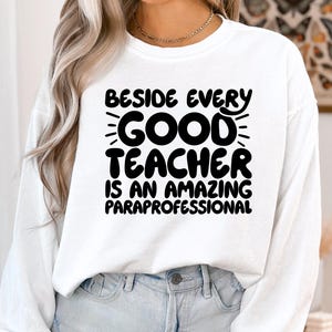 May include: White long-sleeved sweatshirt with black text that reads "Beside every good teacher is an amazing paraprofessional".