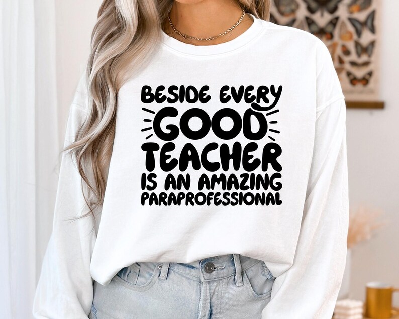 May include: White long-sleeved sweatshirt with black text that reads "Beside every good teacher is an amazing paraprofessional".