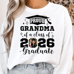 Peut inclure: Sweat-shirt blanc avec l'inscription "PROUD GRANDMA of a class of 2026 Graduate". Le motif comprend un chapeau de graduation et une photo d'un dipl&ocirc;m&eacute;. Le sweat-shirt est de style d&eacute;contract&eacute; et confortable.
