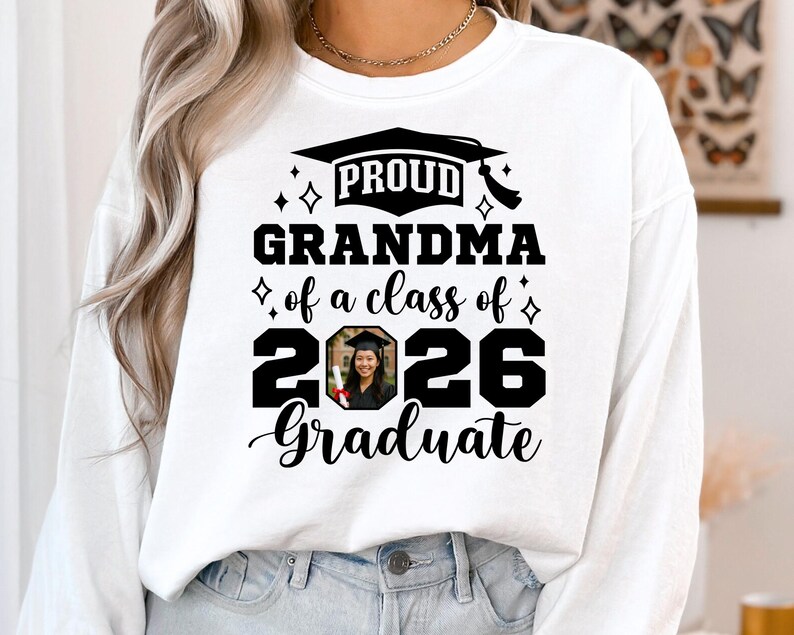 Peut inclure: Sweat-shirt blanc avec l'inscription "PROUD GRANDMA of a class of 2026 Graduate". Le motif comprend un chapeau de graduation et une photo d'un dipl&ocirc;m&eacute;. Le sweat-shirt est de style d&eacute;contract&eacute; et confortable.