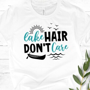 May include: White t-shirt with a black graphic that says "lake hair don't care". The graphic also includes a sun, birds, a canoe, and waves.