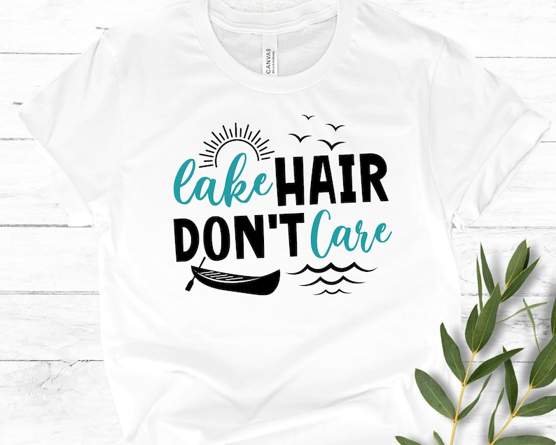 May include: White t-shirt with a black graphic that says "lake hair don't care". The graphic also includes a sun, birds, a canoe, and waves.