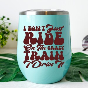 May include: A turquoise stainless steel wine tumbler with a brown graphic that reads "I don't just ride on the crazy train I drive it"