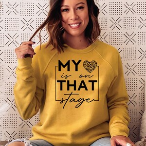 May include: A yellow sweatshirt with the text "MY &hearts; is on THAT stage" in black lettering. The heart has a leopard print pattern.