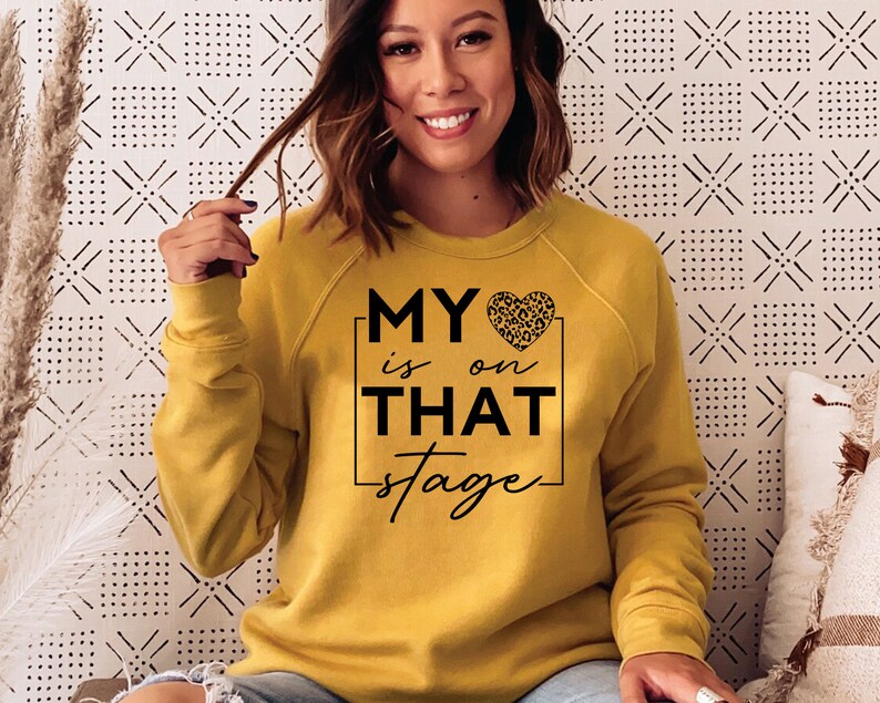 May include: A yellow sweatshirt with the text "MY &hearts; is on THAT stage" in black lettering. The heart has a leopard print pattern.