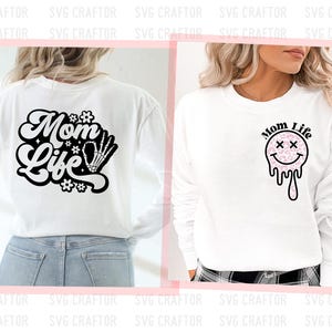 May include: Two white long-sleeve shirts with different designs. The first shirt has a black design that says "Mom Life" with a skeleton hand. The second shirt has a black design that says "Mom Life" with a pink and white smiley face.