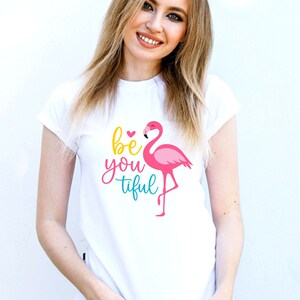 May include: White t-shirt featuring a pink flamingo and the text "be you tiful" in colourful lettering.