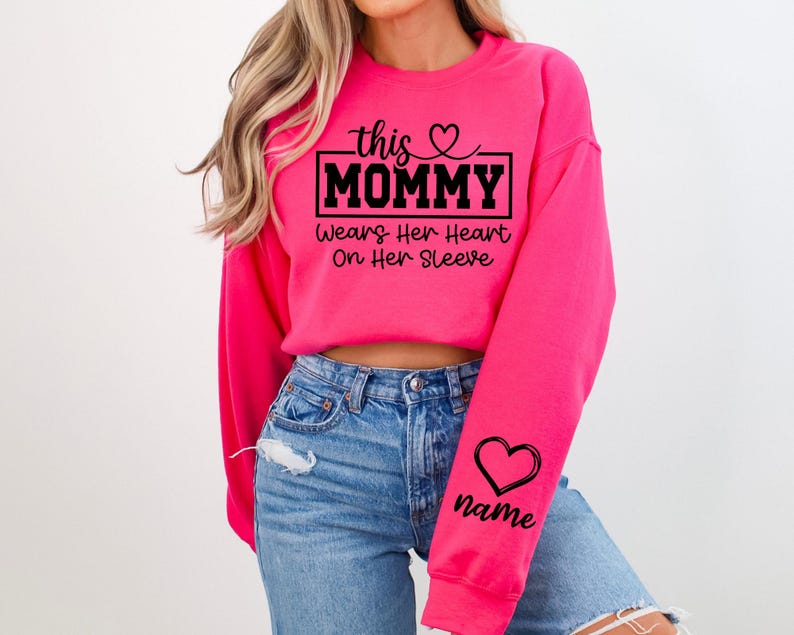 May include: A bright pink sweatshirt with the text "this MOMMY Wears Her Heart On Her Sleeve" in black. A black heart and the word "name" are printed on the sleeve. The sweatshirt is a crew neck style.
