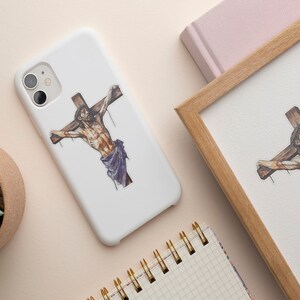 May include: A white phone case with a religious image of a person on a cross. The image is in black, brown, and purple.