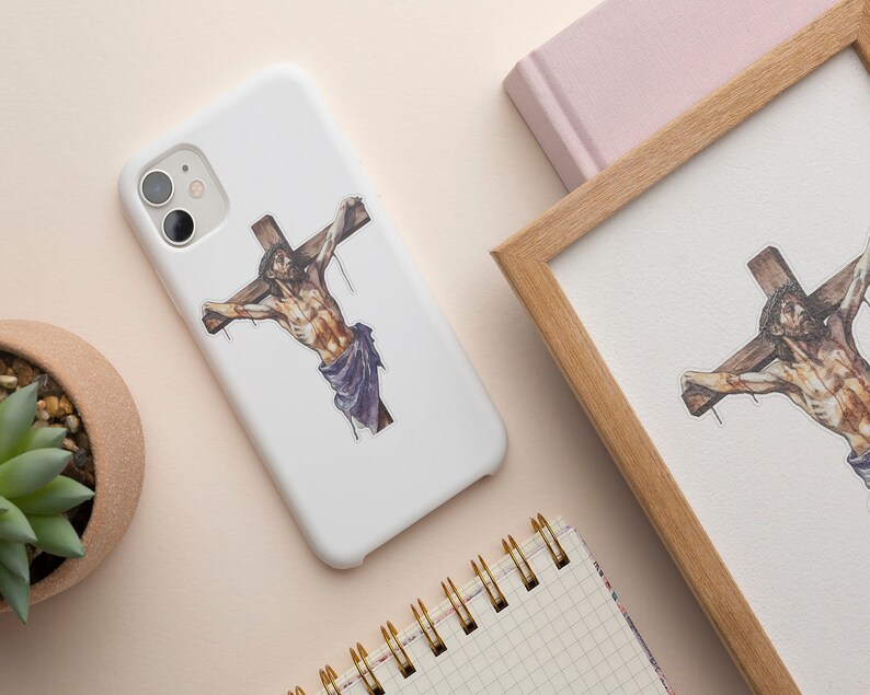 May include: A white phone case with a religious image of a person on a cross. The image is in black, brown, and purple.