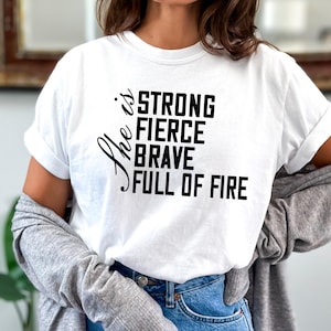 May include: White t-shirt with black text that reads "She is strong fierce brave full of fire".