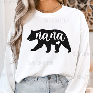 May include: White long-sleeve shirt with a black bear silhouette and the word "nana" in black text. The bear has a small heart on its chest.