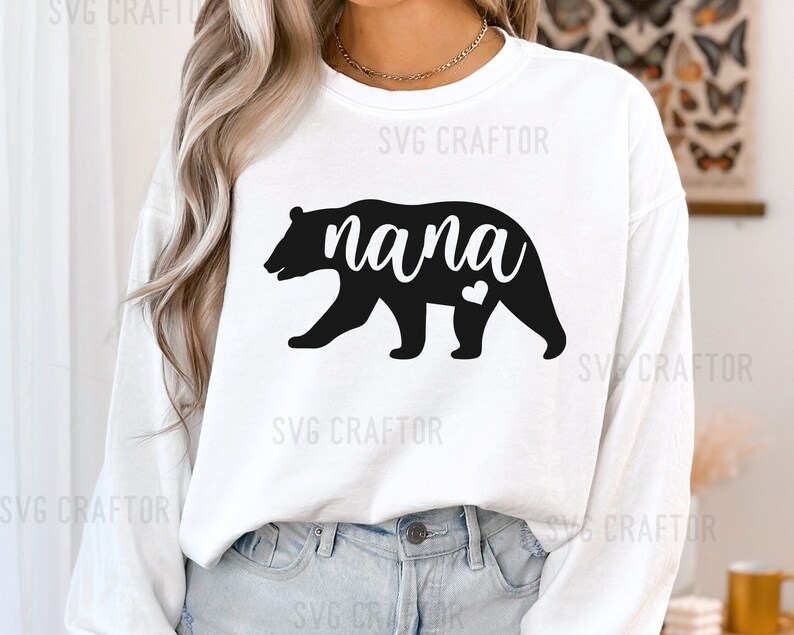 May include: White long-sleeve shirt with a black bear silhouette and the word "nana" in black text. The bear has a small heart on its chest.