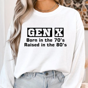 May include: White long-sleeve sweatshirt with black text that reads "GEN X Born in the 70's Raised in the 80's".
