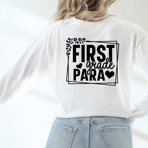 May include: White long-sleeved shirt with black text that reads "FIRST grade PARA" in a box with leopard print accents.