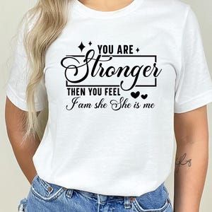 May include: White t-shirt with black text that reads "You are stronger then you feel I am she She is me" with two small black hearts.