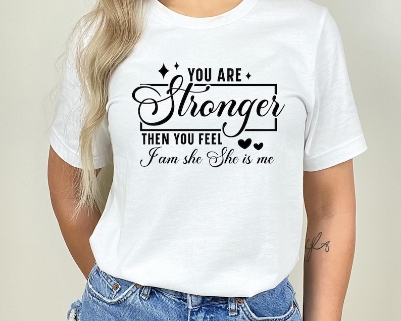 May include: White t-shirt with black text that reads "You are stronger then you feel I am she She is me" with two small black hearts.
