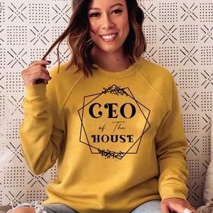 May include: A mustard yellow sweatshirt with black text that reads "CEO of the HOUSE" inside a geometric frame with floral accents.