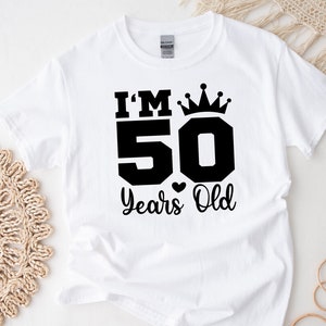 May include: White t-shirt with black text that reads "I'm 50 Years Old" with a crown above the 50.