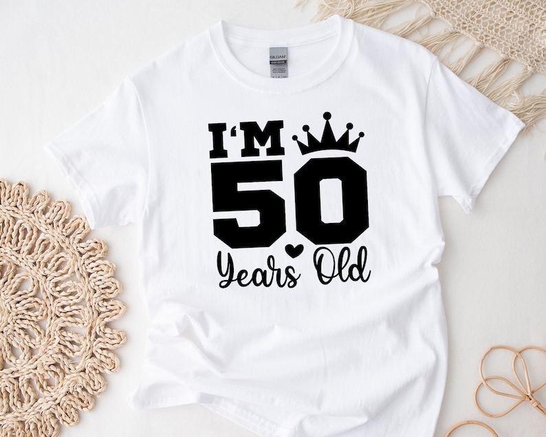 May include: White t-shirt with black text that reads "I'm 50 Years Old" with a crown above the 50.