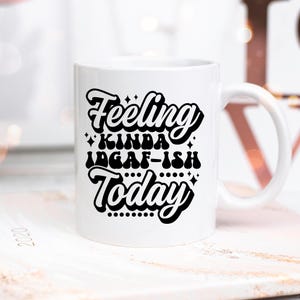 May include: White ceramic coffee mug with a black graphic that reads "Feeling Kinda IDGAF-ish Today".
