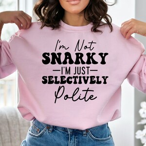 May include: Pink sweatshirt with black text that reads "I'm Not Snarky - I'm Just Selectively Polite"