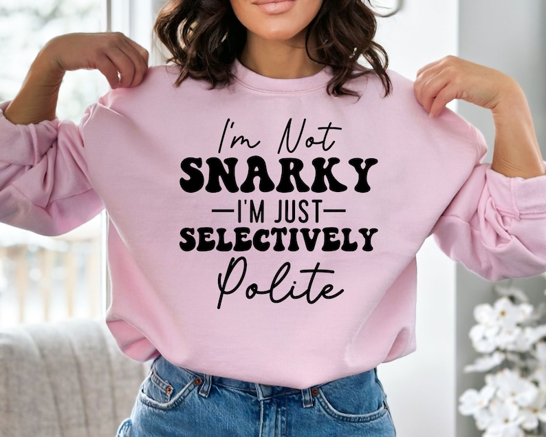 May include: Pink sweatshirt with black text that reads "I'm Not Snarky - I'm Just Selectively Polite"