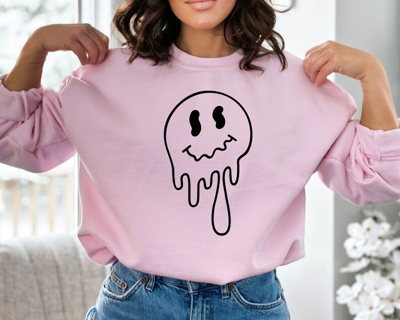 K&ouml;nnte beinhalten: Ein rosa Sweatshirt mit einem schwarzen, tropfenden Smiley-Motiv.